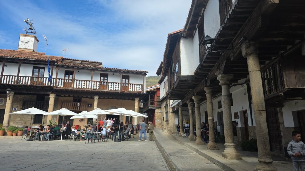 Plaza Mayor de Valverde de la Vera con soportales de granito, balcones de madera y terrazas al sol de otoño