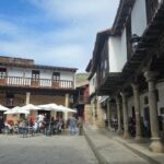 Plaza Mayor de Valverde de la Vera con soportales de granito, balcones de madera y terrazas al sol de otoño