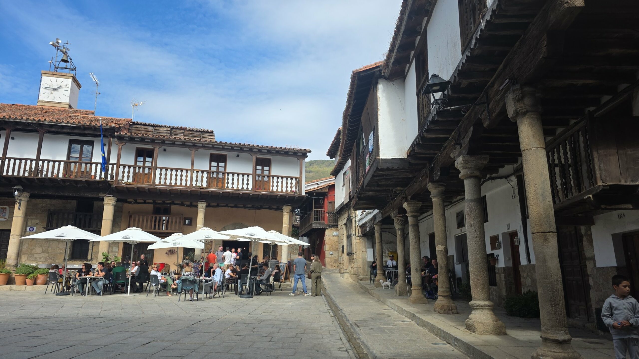 Plaza Mayor de Valverde de la Vera con soportales de granito, balcones de madera y terrazas al sol de otoño